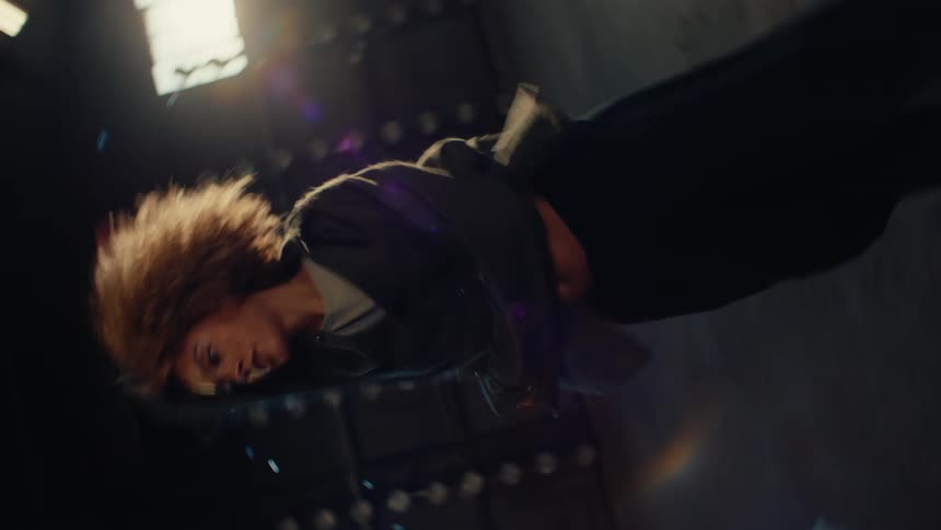 An expressive female dancer with an afro performs a dynamic contemporary routine in a vast, sunlit industrial warehouse in slow motion
