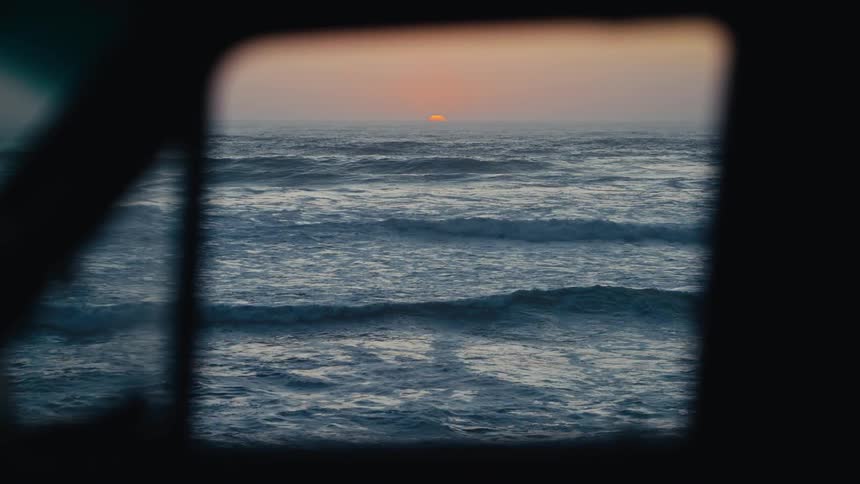 A framed view of rolling ocean waves as the sun sets on the horizon
