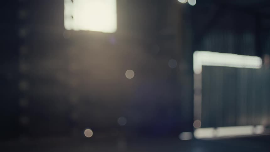 A beautiful woman with a large blonde afro is backlit as she walks through a dark, moody industrial space in slow motion