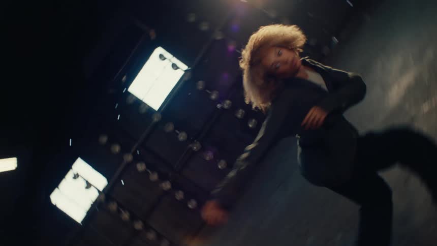 Dynamic slow motion footage captures a stylish woman performing an expressive contemporary dance in a vast, sun-drenched industrial warehouse