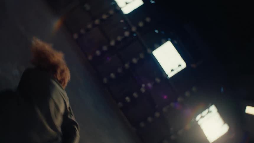 In a surreal slow-motion sequence, a woman falls from the ceiling and lands gracefully, beginning a contemporary dance in a vast, empty warehouse