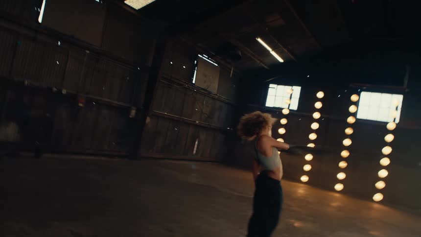 Slow motion shot of a stylish female dancer with an afro performing an expressive contemporary dance in a moody, empty warehouse