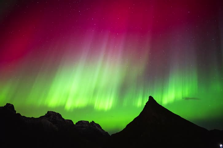 A stunning time-lapse of vibrant green and magenta Northern Lights dancing in the starry night sky over a silhouetted mountain peak