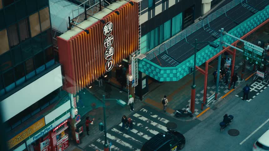 A high-angle view of a bustling street corner in Tokyo, Japan, where pedestrians cross under a glowing sign