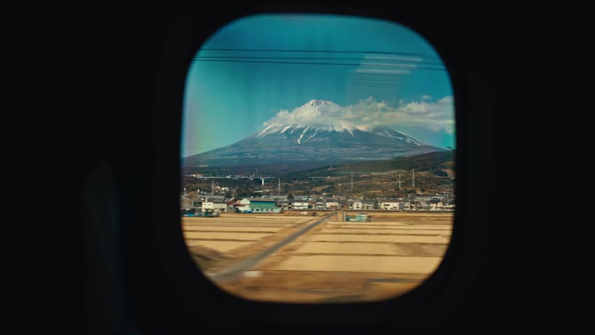 A scenic view of the snow-capped Mount Fuji from the window of a moving bullet train in Japan