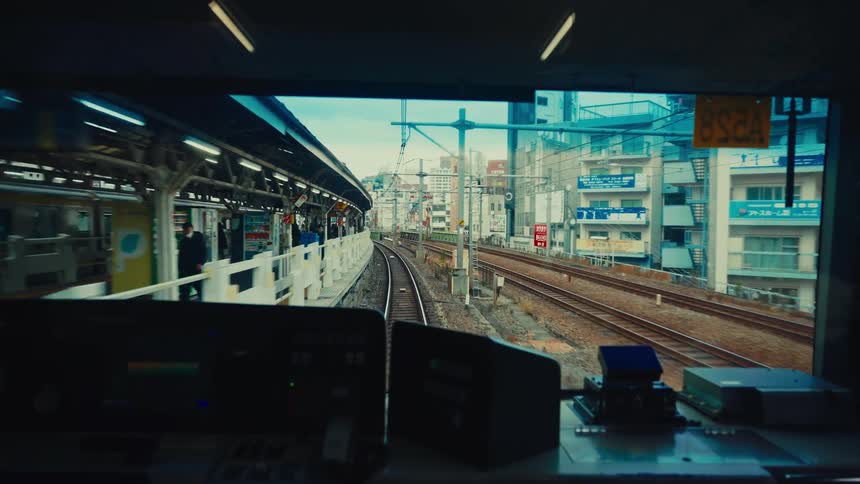 A cinematic point-of-view shot from the front of a train departing a station in a Japanese city