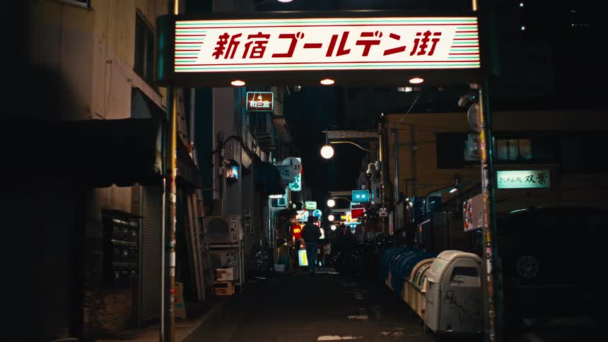 A static view down a narrow alley at the entrance to Shinjuku Golden Gai in Tokyo, with vibrant neon signs illuminating the street at night