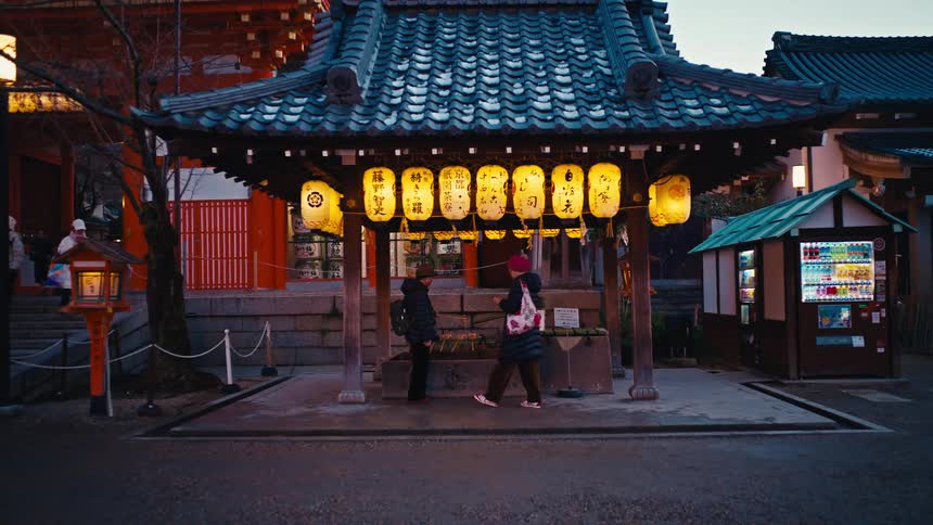 Visitors stand beneath glowing paper lanterns at a traditional Japanese shrine during the quiet evening hours
