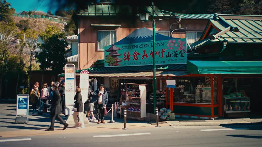 A group of people wait at a bus stop while others walk past a traditional souvenir shop on a bustling street in Japan
