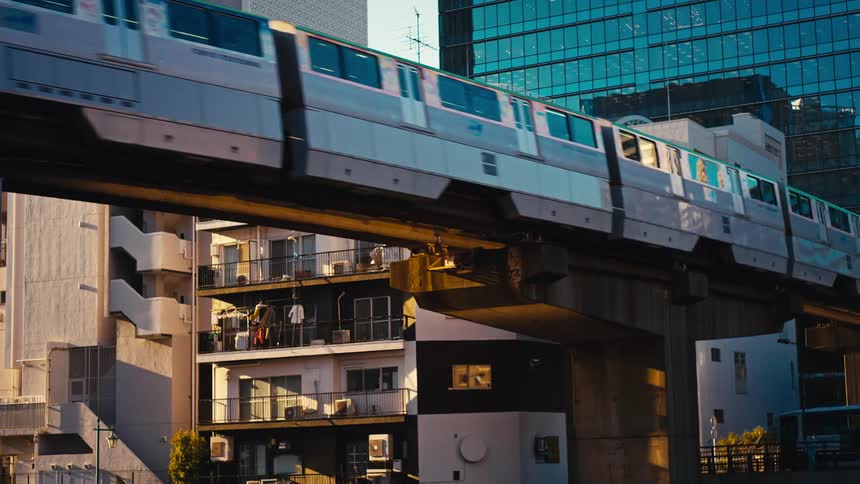 A monorail train glides along an elevated track through a dense cityscape, juxtaposing modern skyscrapers with older residential apartments