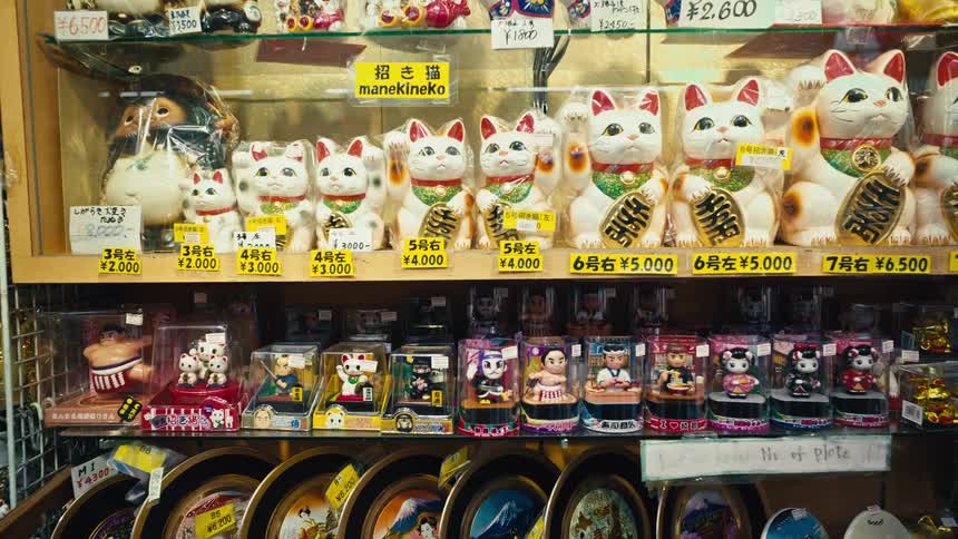 A shelf in a Japanese souvenir shop is filled with Maneki-neko lucky cats and other traditional figurines for sale