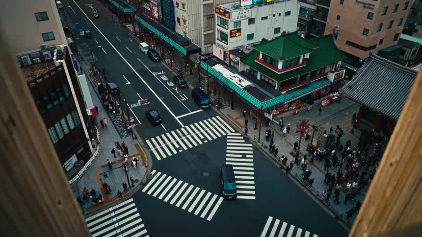 A framed, high-angle view captures the bustling street corner of Asakusa, Tokyo, as cars and pedestrians navigate the intersection