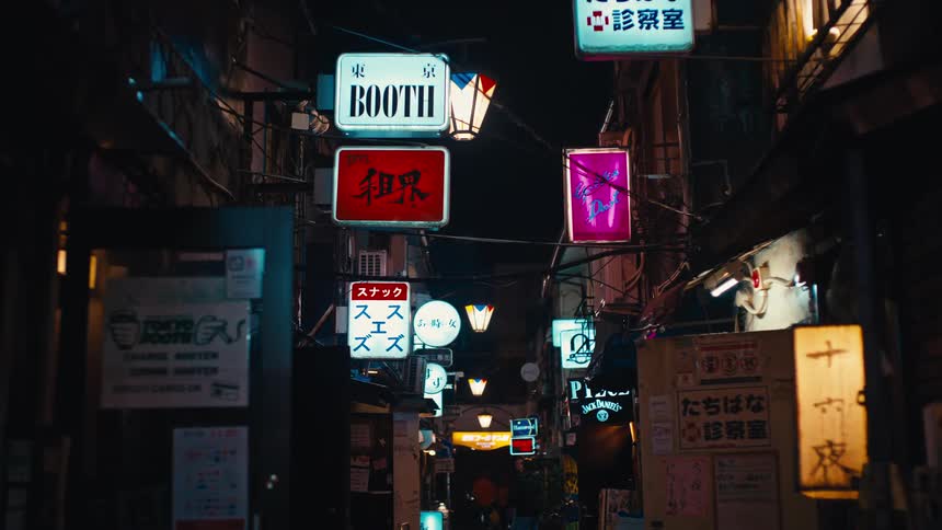 A narrow, moody back alley in Tokyo glows with a dense collection of illuminated signs at night