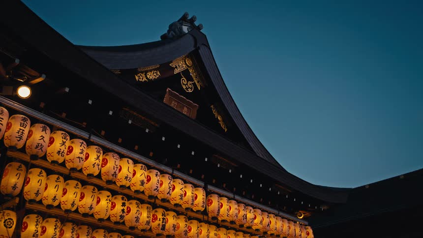 Rows of glowing Japanese paper lanterns illuminate a traditional temple against the deep blue dusk sky