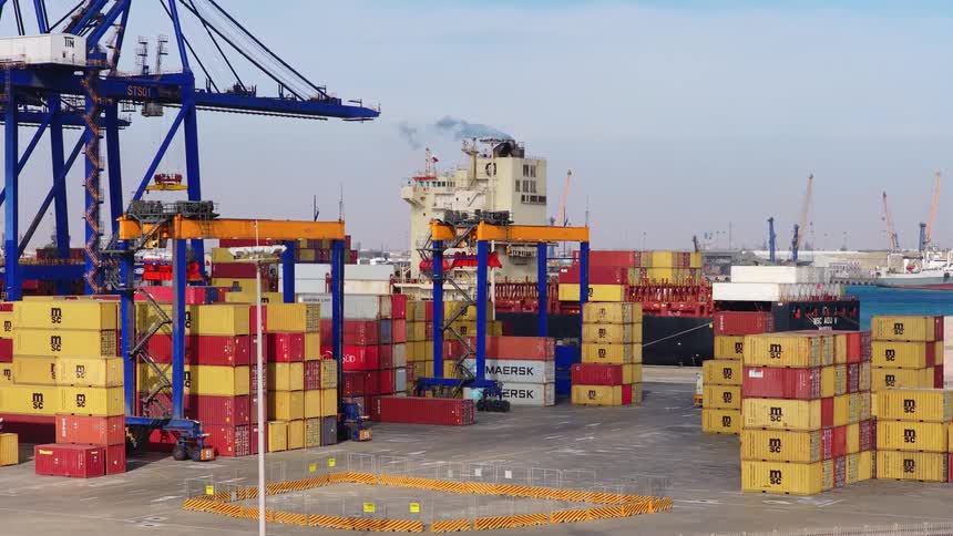Busy container terminal with large gantry cranes loading and unloading colorful shipping containers from a cargo vessel