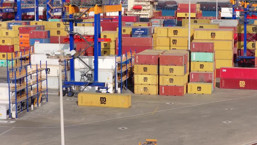 A straddle carrier maneuvers between stacks of colorful shipping containers at a bustling industrial port