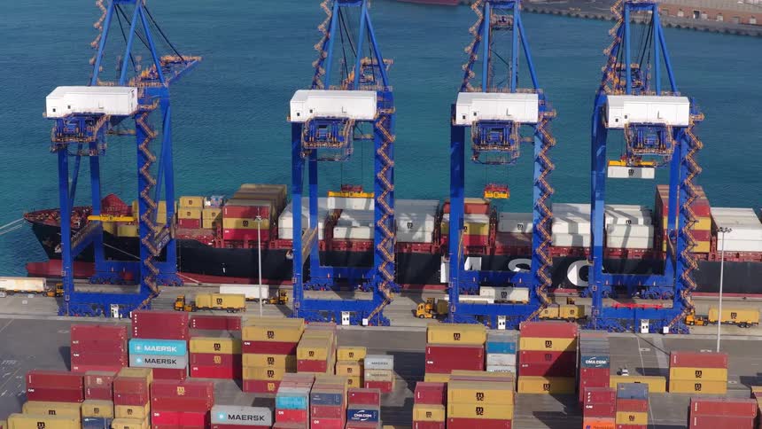 Large gantry cranes load and unload a massive container ship docked at a busy industrial shipping port