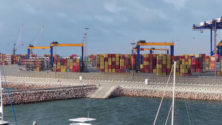 A view from a departing boat of a massive industrial shipping port with stacks of containers and operating gantry cranes