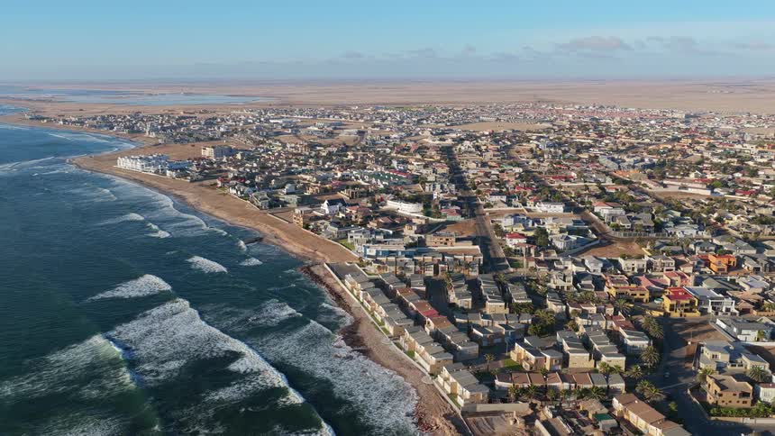A stunning static aerial view captures the unique landscape of a coastal town nestled between the crashing waves of the ocean and the expansive desert