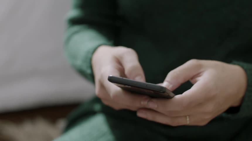 A woman sitting in a room during the day is texting on her cellphone