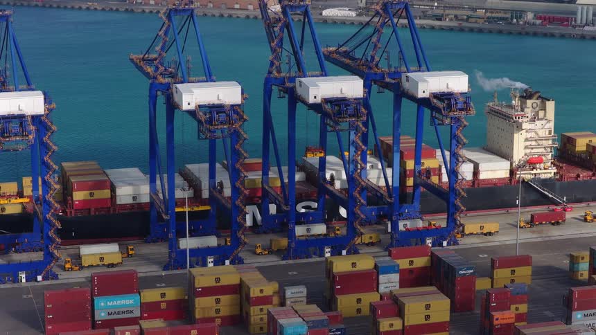Massive blue gantry cranes actively load and unload colorful shipping containers from a large cargo ship at a bustling industrial port