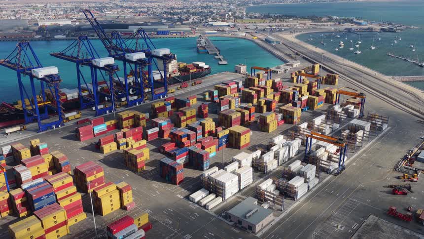 An expansive, static aerial view showcases a major shipping port, complete with colorful cargo containers, large cranes, and a docked vessel