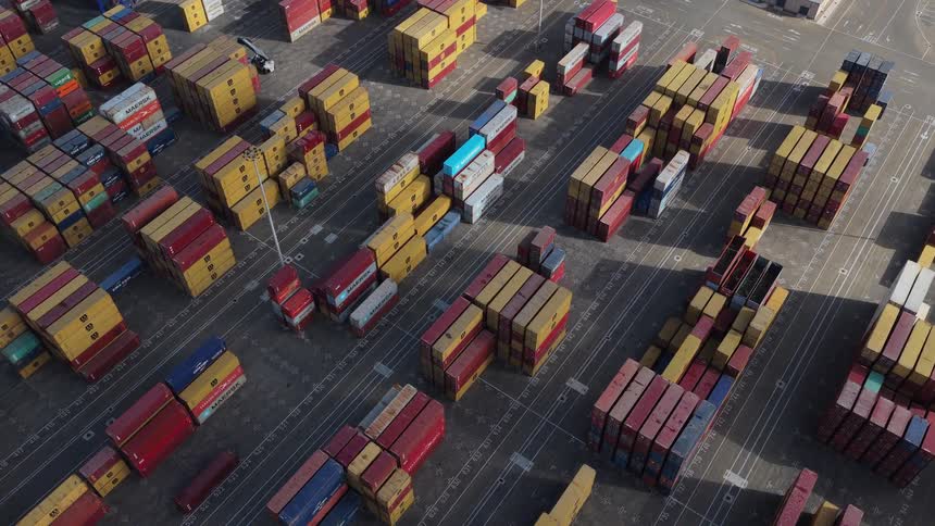 Rising aerial view of a large container terminal where thousands of colorful cargo containers are stored and organized for international shipping