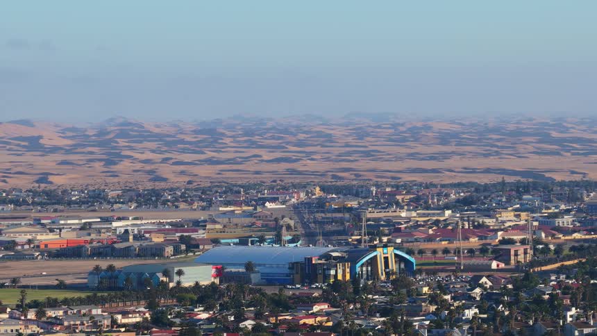 Wide, high-angle view of the coastal town of Walvis Bay, Namibia, with the vast dunes of the Namib Desert stretching to the horizon