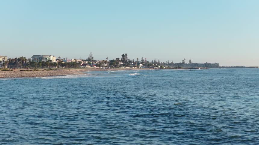 A scenic wide shot of the calm ocean lapping against the shoreline of a coastal town on a clear day