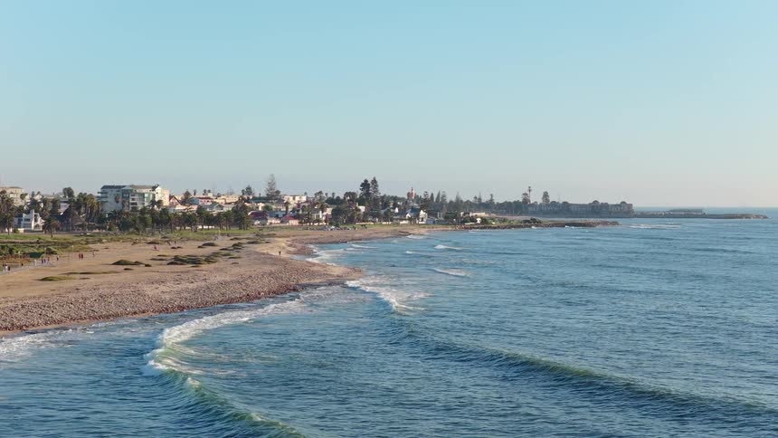 Slow-motion waves gently break on the shore of a peaceful coastal town on a bright sunny day