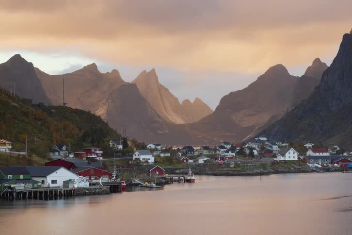 A stunning timelapse of golden sunlight breaking through clouds to illuminate a picturesque Norwegian fishing village nestled between majestic mountains