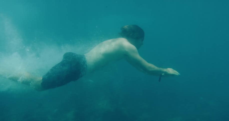 Underwater slow motion view of a man gracefully diving and swimming through the tranquil sea