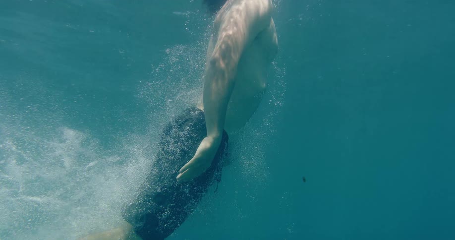 Underwater slow-motion view of a young man diving into the tranquil sea, creating a trail of bubbles