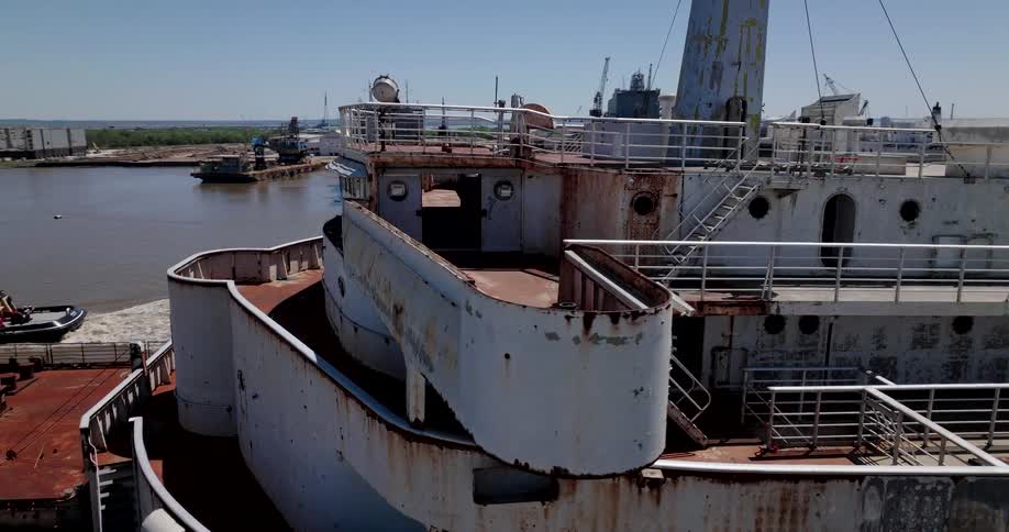 An aerial view slowly explores the decaying and rusty decks of the historic SS United States ocean liner docked in an industrial port