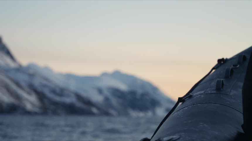 An inflatable Zodiac boat drifts on calm arctic waters with majestic snow-covered mountains in the distance