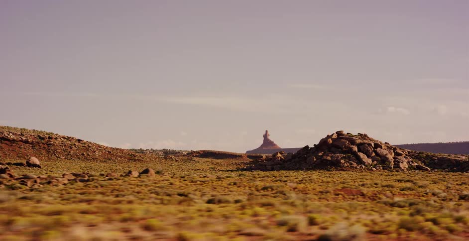 A wide driving plate shot captures the vast, arid desert landscape of the American West with a distant butte on the horizon