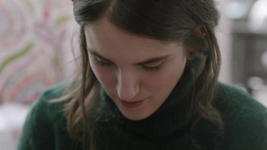 A woman wearing a green sweater is using a phone