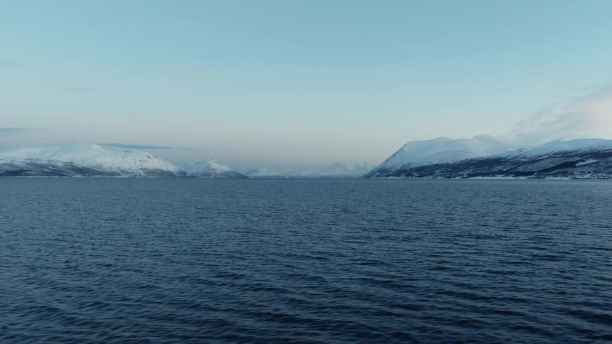 A serene, wide shot of a tranquil arctic fjord with majestic snow-covered mountains in the distance