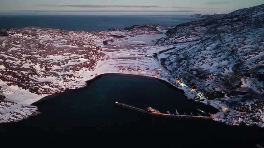 A serene aerial view of a small coastal village nestled in a snowy bay during a tranquil winter twilight