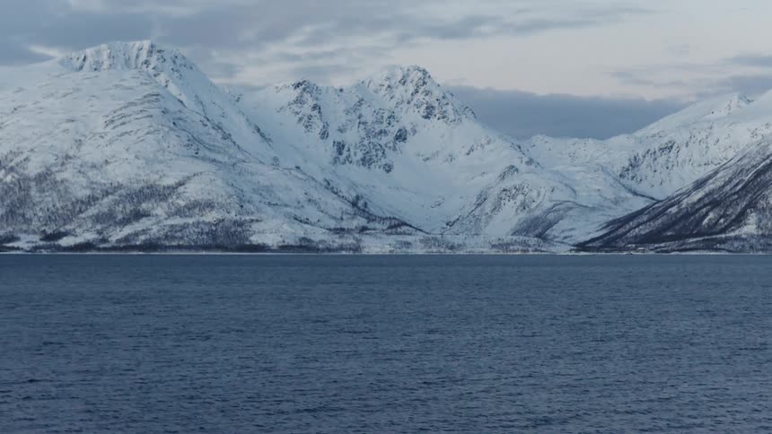 A tranquil wide shot of a majestic snow-covered mountain range across a calm body of water