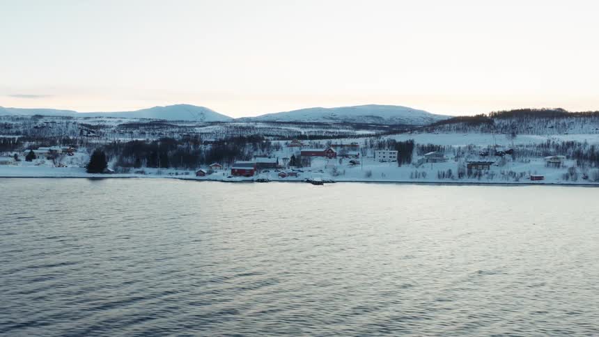A serene view from the water of a snow-covered coastal village in Norway during a quiet winter day