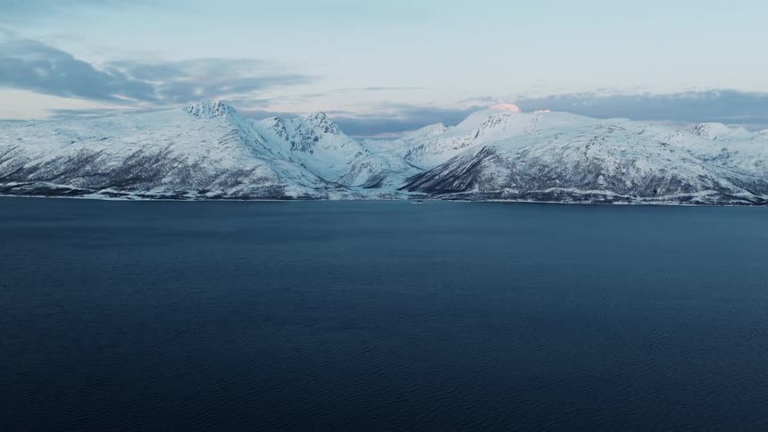 A serene aerial view of a calm fjord with majestic snow-covered mountains in the background during a winter sunrise