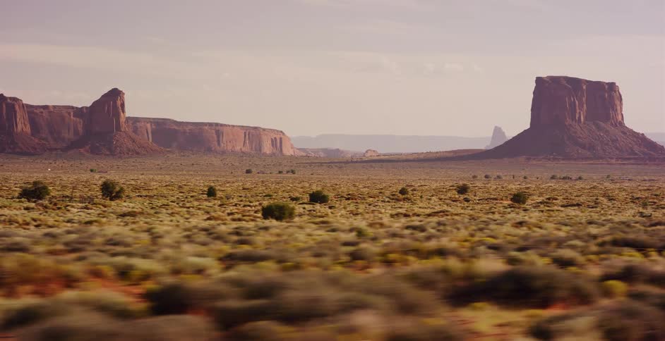 A stunning drive-by view captures the majestic red rock buttes and mesas of Monument Valley across a vast desert plain