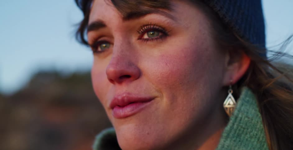 An emotional close-up of a woman with tears in her eyes as she looks off into the distance during a beautiful sunset