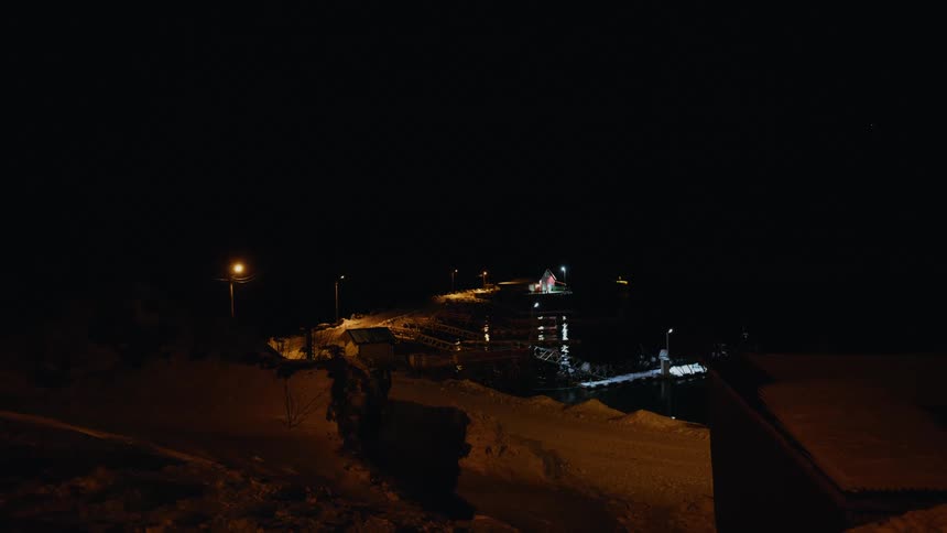 A quiet, snowy harbor illuminated by warm lights on a dark winter night