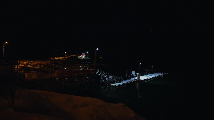 A rescue team conducts a training exercise on a pier at night, lowering a person into the dark water below