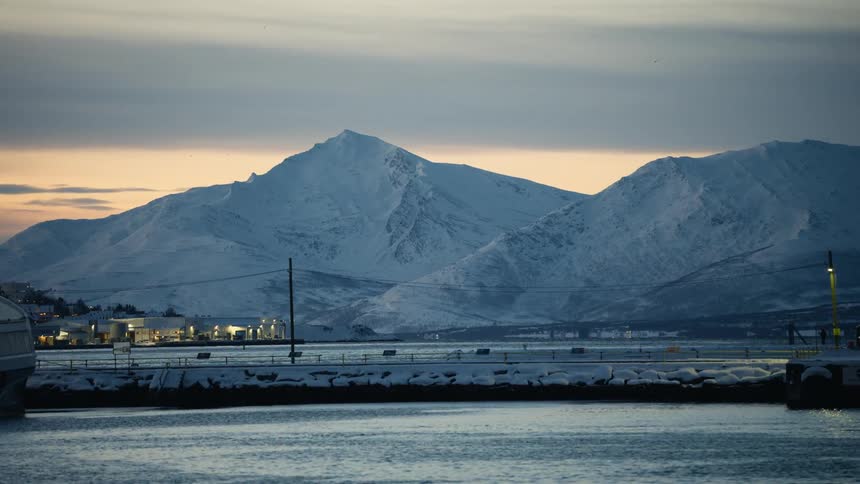 Majestic snow-covered mountains tower over a tranquil harbor at twilight