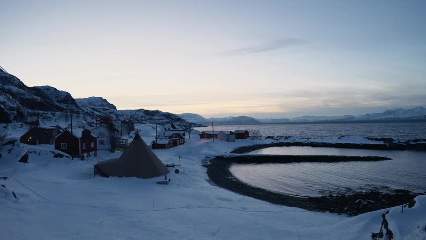 A tranquil winter scene shows a snow-covered coastal village with a traditional Sami lavvu tent by the water at dusk