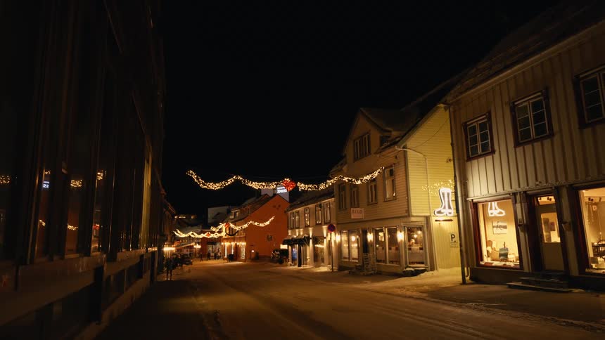 A charming, snow-covered street in a Nordic town is beautifully decorated with festive lights for the Christmas holidays