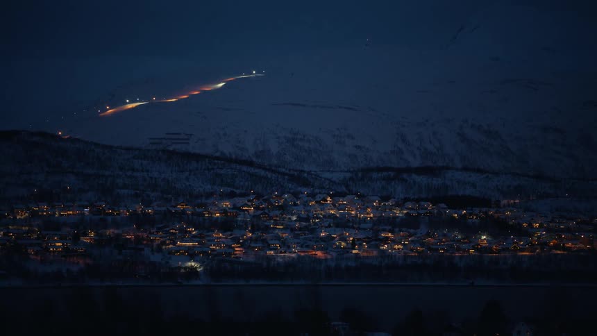 Nighttime timelapse of a cozy town glowing in a snowy mountain valley with a lit-up ski slope winding up the hillside
